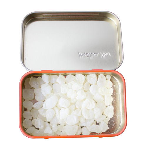 Open tin of Chios mastic gum pieces on a white background